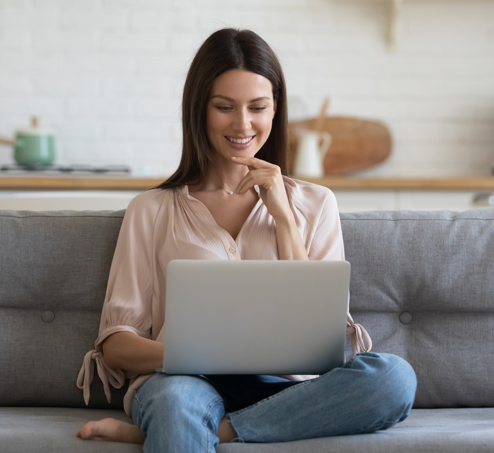 Photo of woman on couch smiling and looking at laptop